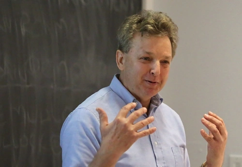 Richard Ingersoll gestures with both hands, standing in front of a chalkboard