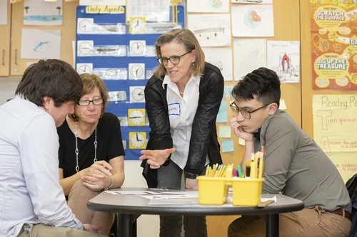 Dr. Caroline Ebby stands over three adults sitting at a table and discusses responsive math.