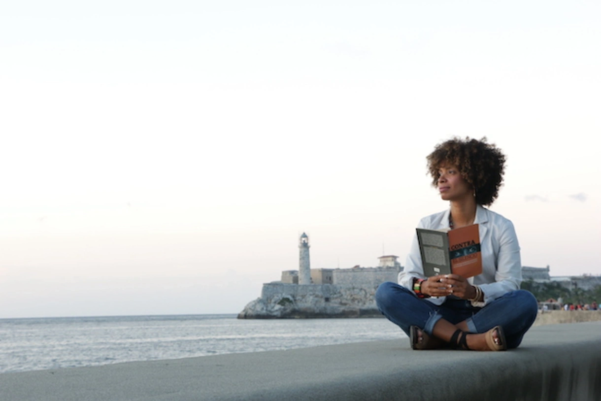 Amalia Dache sits on a ledge overlooking a harbor during a research trip to Cuba.