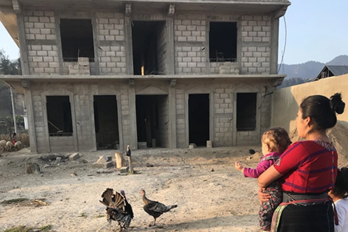Woman holding a child looking at a two-story home under construction.