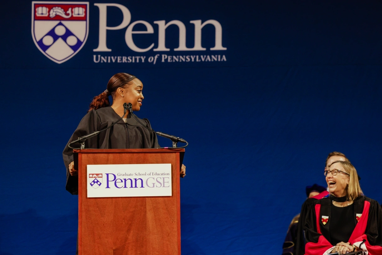 Abbott Elementary creator Quinta Brunson stands at a podium sharing a laugh with Penn GSE Dean Pam Grossman, seated to her right.