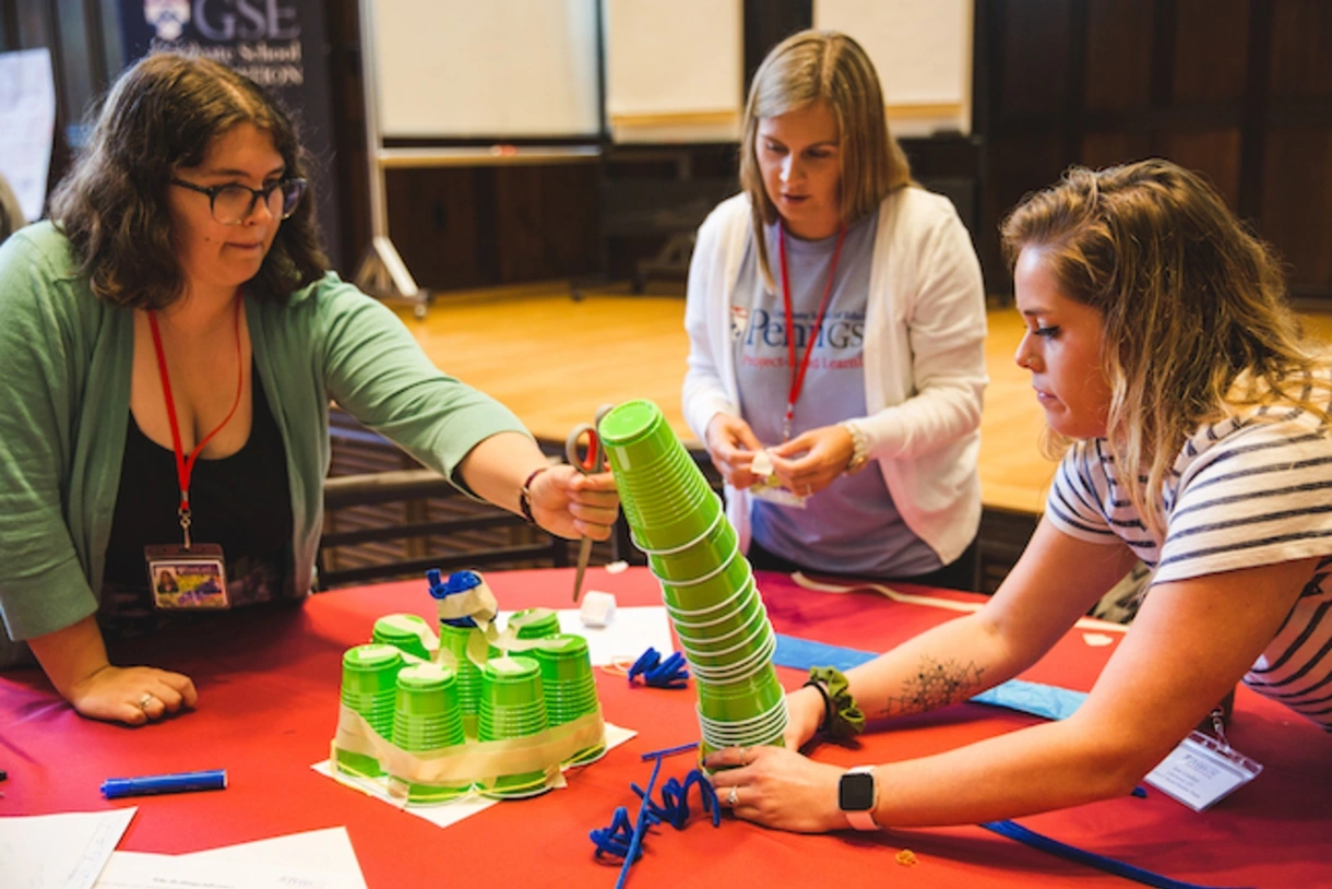 A group of educators attempts to stack cups on a table during a project-based learning professional development workshop.