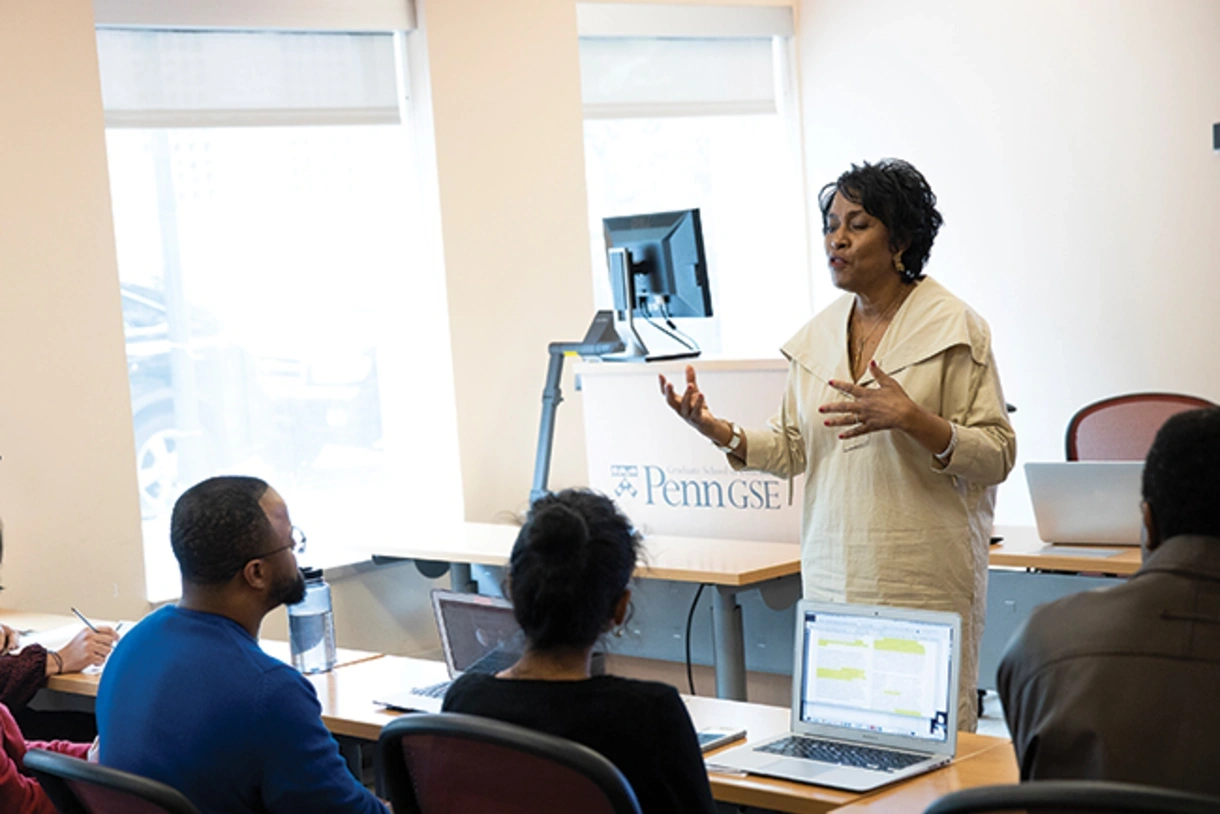Professor Gadsden addresses graduate students who are listening intently with laptops or notepads open in front of them, in a bright classroom.