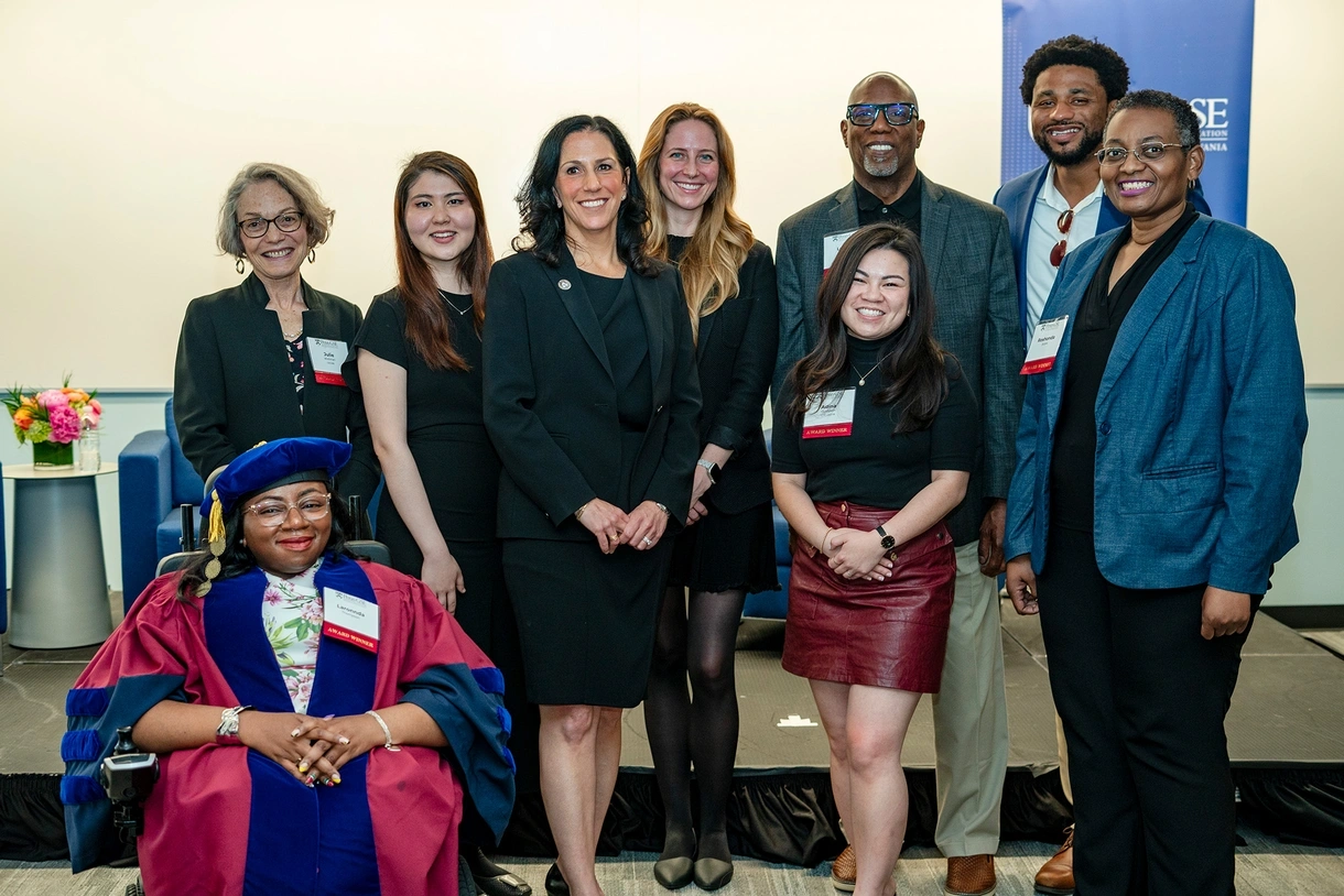 Nine award winners, including one in her red-and-blue graduation tam and gown, pose onstage with the dean after the 2024 Celebration of Educators event.