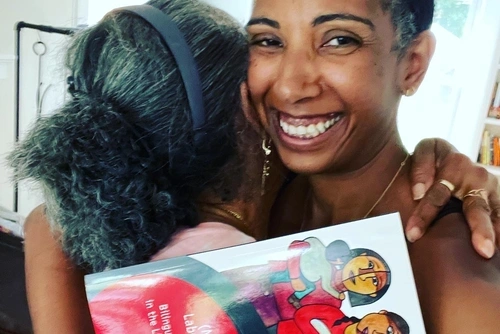 women smiling while hugging someone and holding a book