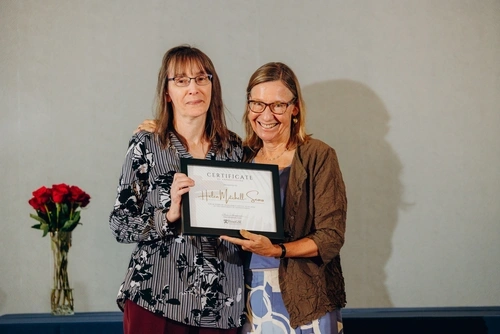 Dean Pam Grossman has her arm around Helen Mitchell-Sears as they both hold the Certificate of Appreciation being bestowed to Sears