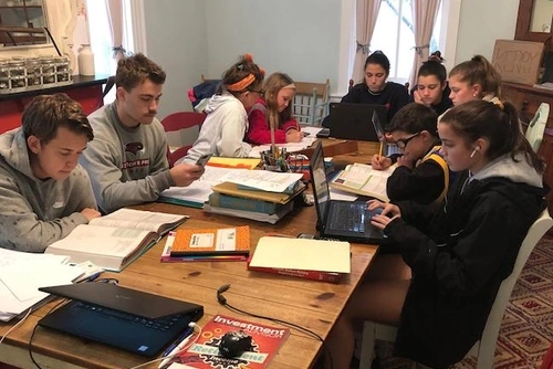 A family crowds around a dining room table working on homework.