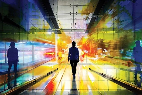 Silhouette of a woman walking through a tunnel of glass that reflects different colors of scattered