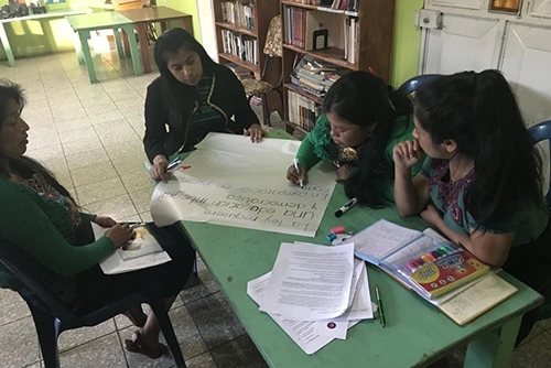 Women sitting around a table in a classroom environment investigating documents.