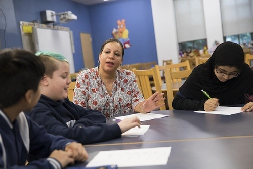 A teacher and students sit around a table, before COVID-19.