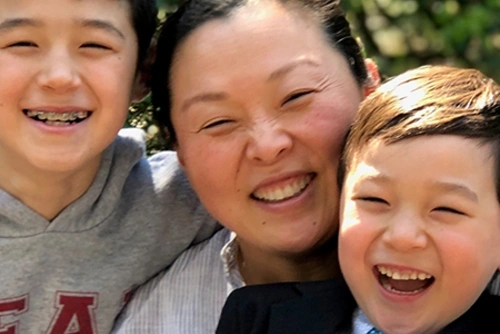 Melissa Kim smiles in between two smiling children outdoors