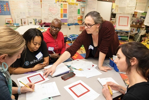 Four students work together on a paper assignmenr while a faculty member reviews their work