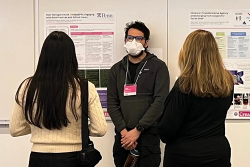 A man stands in front of a poster on the wall describing his research to two conference attendees.
