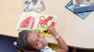 A girl looks up from reading a picture book. 