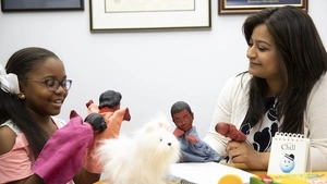 A student and a school counselor use dolls during a counseling session.