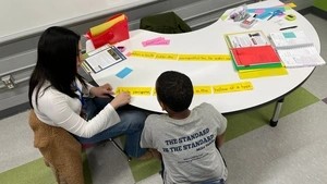 Penn Arts & Sciences undergrad Sarah Alvarado tutors a Hamilton Elementary student in reading at a small table in a classroom
