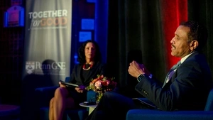 Superintendent Watlington speaks, seated in the foreground, as Dean Strunk, seated in the background in front of a “Together for Good: Penn GSE” banner, listens.