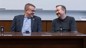 Representatives Bryan Cutler and Peter Schweyer sit at a table in front of a white board and face each other, laughing.