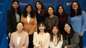 10 Penn students pose for a photo, four seated and six standing behind them, in front of a Wharton AI + Analytics background