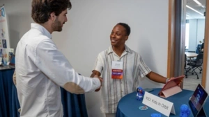 An alumni founder shakes the hand of another alum in front of the table for his venture, KIO: Kids in Orbit, which features iPads and small spaceman figurines