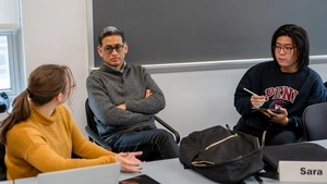 Rand Quinn sits at a table with his arms crossed engaged in discussion with two students